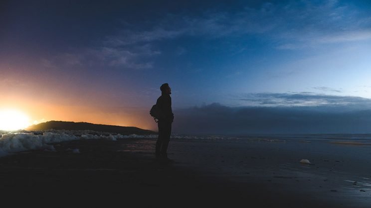 مردی میان غروب آفتاب و طلوع مهتاب در ساحل ایستاده
